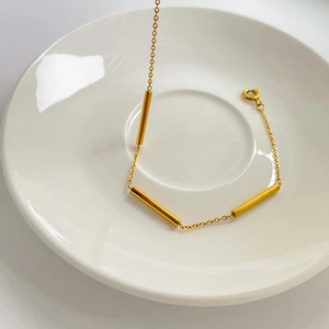 Minimalist gold cylindrical tube chain bracelet displayed in a white ceramic dish