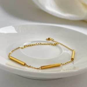 Detailed close-up of golden tubular beads and delicate link chain with lobster clasp