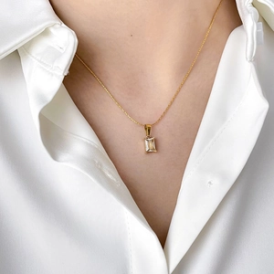 Close-up of gold chain necklace with square crystal pendant on white shirt