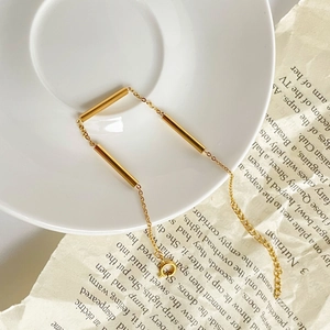 Close-up of minimalist gold cylinder tube chain bracelet on vintage paper and white plate