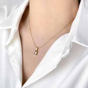 Close-up of elegant gold necklace with rectangular clear crystal on a model wearing silk