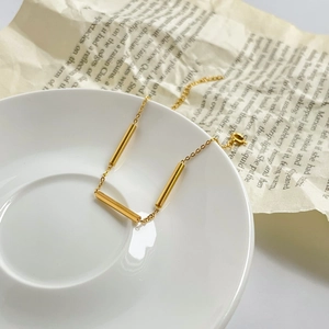 Close-up of minimalist gold bar chain bracelet on a ceramic dish with vintage paper