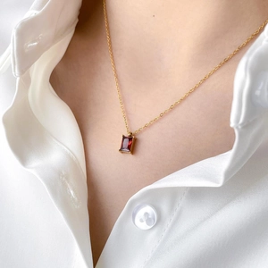 Detail of a square cut red crystal pendant necklace worn on a gold chain
