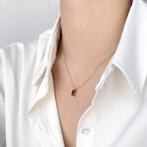 Close-up of minimalist gold necklace with rectangular red gemstone on a model
