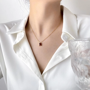 Close-up of a gold necklace with a rectangular red gemstone on a model in white silk