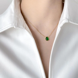 Gros plan d'un collier avec pendentif goutte verte porté sur un col de chemise blanche chic
