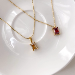 Close-up of elegant gold necklaces with emerald-cut red and champagne square crystals