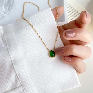 Gros plan d'un pendentif en agate verte en forme de poire sur une fine chaîne dorée
