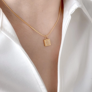 Gros plan d'un collier chaîne serpent dorée avec pendentif œil de chat carré sur un modèle