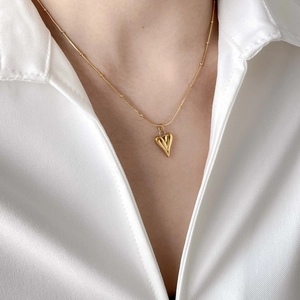 Nahaufnahme einer goldenen Herzanhängerkette an einem Modell in weißem Hemd