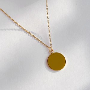 Macro shot of polished gold round pendant necklace with fine chain on white texture