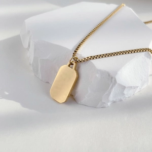 Close-up of minimalist gold plated box chain necklace with sleek rectangular tag on white stone