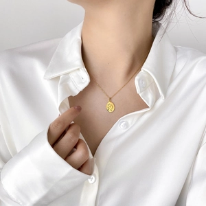 Close-up of a gold celestial coin pendant necklace with diamonds on a white silk shirt