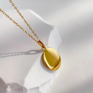 Detail of minimalist gold oval pendant with high-polished mirror finish on white stone