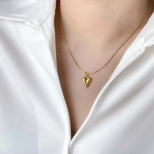 Nahaufnahme der minimalistischen goldenen Herz-Halskette an einer Gliederkette vor weißem Hemd