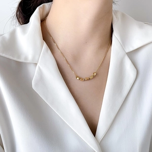 Close-up of a warm gold necklace with five bean pendants worn on a white collared shirt