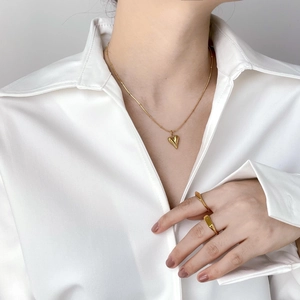 Minimalistisches Set aus goldener Herzkette und Ringen auf weißem Seidenhemd