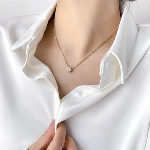 Detail shot of a minimalist gold zircon pendant necklace on a female wearer in a white shirt