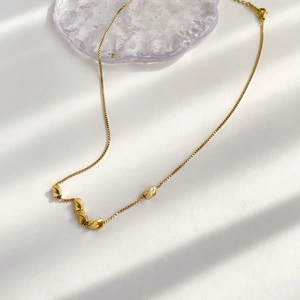 Detail of minimalist gold bead necklace with irregular pendants on a square link chain