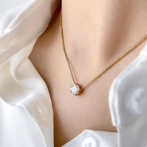 Detail of a minimalist gold box chain necklace with a sparkling round zircon pendant