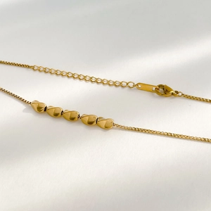 Detail of gold box chain necklace with five polished heart charms and adjustable lobster clasp