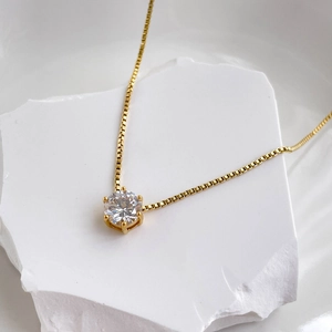Close-up of golden box chain necklace with single round cubic zirconia in six-prong setting