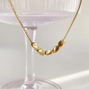 Minimalist gold box chain necklace with five polished twisted beads on glass background