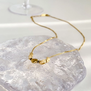 Detailed macro view of the gold bean pendant and fine box chain on an ice texture base