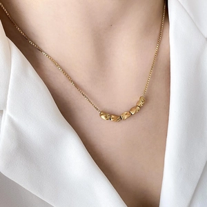 Detail of gold bean pendant on box chain worn with a white blazer for a minimalist look