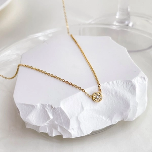 Detailed view of a gold sunburst pendant with zircon inlay on a white textured stone