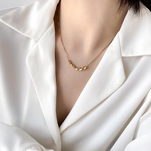 Macro shot of minimalist gold lucky bean necklace worn over a white silk shirt