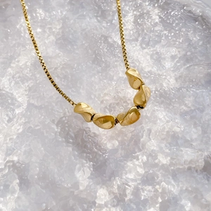 Macro detail of 18K gold necklace with irregular fluid charms on a crystalline base