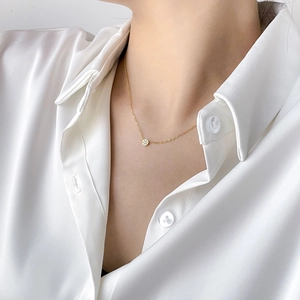 Close-up of a delicate gold chain necklace with a round logo pendant on a silk blouse