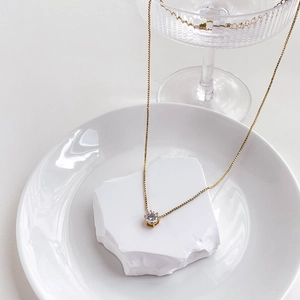Detailed close-up of a single zircon pendant on a gold box chain atop a white stone