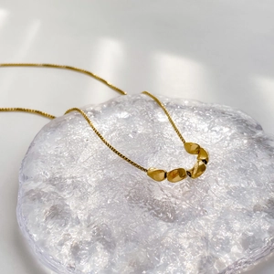 Macro shot of gold bead necklace on ice cube prop with polished box chain link detail