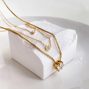 Three-layer gold zircon necklace set with solitaire pendants on a textured stone