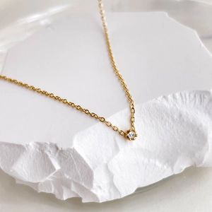 Close-up of a delicate gold chain necklace with a single sparkling zircon pendant