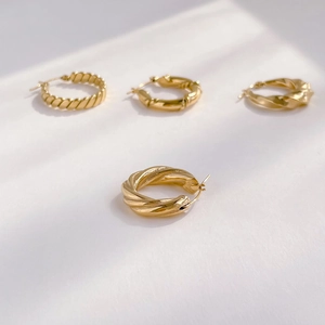 Macro detail of four minimalist gold twisted hoop earrings with elegant light shadows