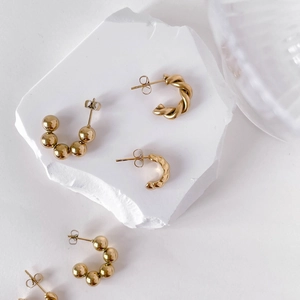 Minimalist gold twist hoop earrings with beads and wave texture on white stone