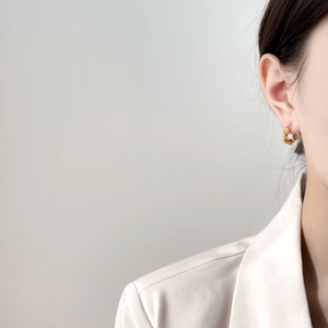 Close-up of elegant golden twisted hoop earrings worn by a model in a white blazer