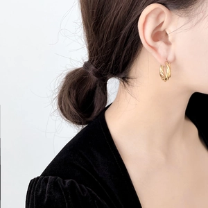 Detail of a minimalist gold-colored twisted hoop earring worn by a model
