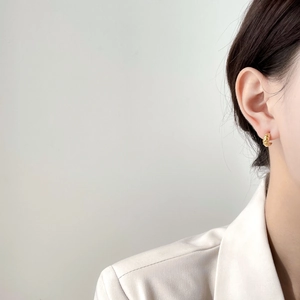 Close-up of elegant gold twist hoop earring worn by a model in a white blazer