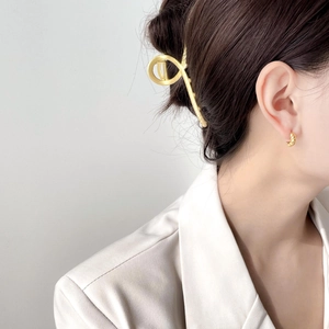 Minimalist twisted gold earrings and geometric hair clip worn by a model in a suit