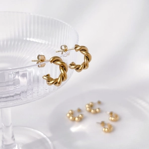 Detailed view of golden twisted rope C-hoop earrings hanging on a textured glass