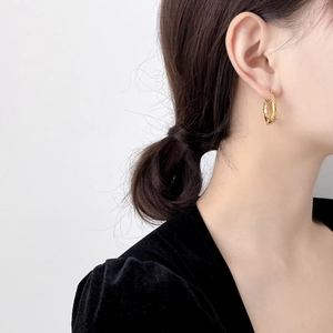 Detail of twisted gold bamboo-style hoop earring on a model with high-shine metallic finish