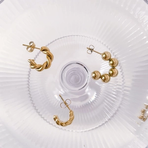 Detailed view of gold twisted, beaded, and spiral hoop earrings on a glass tray