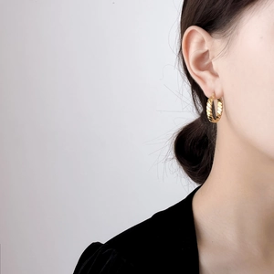Detail of twisted rope gold hoop earrings worn by a model in a minimalist style