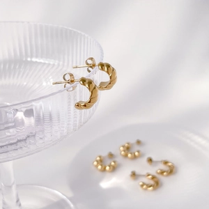 Close-up of golden twisted C-shaped earrings hanging on a textured glass rim