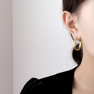Detailed close-up of a twisted rope hoop earring in gold finish on model's ear