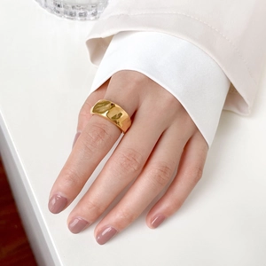 Close-up of a wide gold ring with irregular wavy texture on a model hand